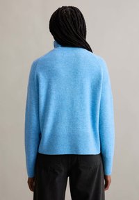 Hellblauer Pullover mit hohem Kragen, strukturiertem Strick, gerippten Bündchen und Saum. Getragen mit dunklen Jeans, die einen lässigen Stil unterstreichen.