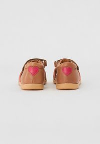 Bruna läderskor för barn med rosa accenter och hjärtformade detaljer bak, med en mjuk, flexibel sula och justerbara remmar.