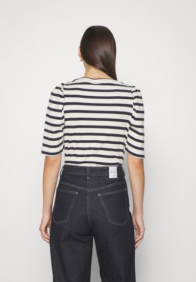 Striped shirt featuring navy and white colors, ribbed texture, short puff sleeves, paired with high-waisted dark denim pants.