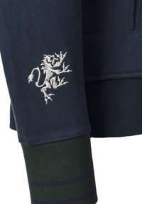 Mörkblå sweatshirt med broderat lejonmotiv, ribbade manschetter med gröna och mörkblå ränder samt ett tyg med mjuk textur.