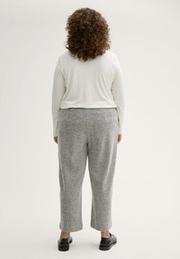Top blanco ligero de manga larga combinado con pantalones grises de patrón espiga y zapatos negros, visto desde atrás.