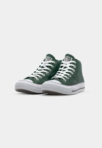 Ténis verdes de cano alto com atacadores brancos, material de tela, sola de borracha, faixa cinza em contraste e um patch de logo na língua.