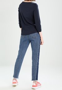 Námořnické tričko s dlouhým rukávem, džíny s světlým washem a tmavým bočním pruhem, roztrhaný lem, nošeno s růžovými teniskami se bílými pruhy.