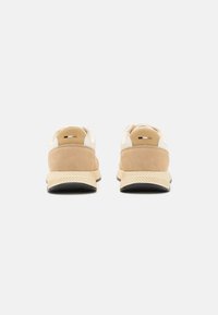 Tan suede and cream leather shoes with a textured rubber sole, featuring rounded backs and minimal branding.