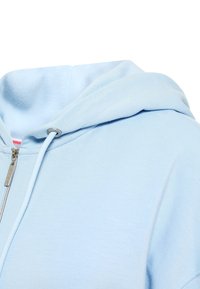 Light blue zip-up hoodie with a drawstring hood, made of soft material. Features a metallic zipper and smooth fabric texture.