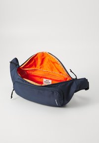 Marineblå skulderveske med oransje innvendig. Mykt, holdbart materiale, har et hovedrom med glidelås og en ekstra frontlomme med glidelås.