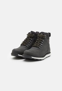 Botas de tobillo impermeables negras con parte superior de cuero texturizado, que presentan ojales de metal, cordones marrones y una suela de goma blanca.