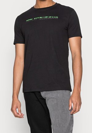Schwarzes Baumwoll-T-Shirt mit Rundhalsausschnitt, kurzen Ärmeln und einem grünen reflektierenden "REPLAY™ BLUEJEANS"-Logo auf der Brust.
