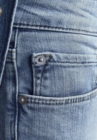 Svijetloplava traper tkanina koja ima mali prednji džep sa srebrnim zatvaračem i vidljive detalje šivanja duž šavova.