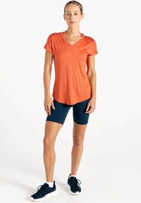 Kurzärmliges, V-Ausschnitt orangefarbenes Sportshirt mit meliertem Muster, kombiniert mit marineblauen Radshorts und schwarzen Sportschuhen.