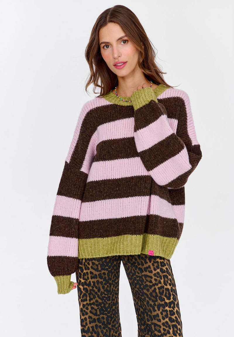 Sweter w paski w różowym, brązowym i zielonym kolorze, z szerokimi rękawami i ściągaczami. Noszony z spodniami w panterkę, z detalem metki.