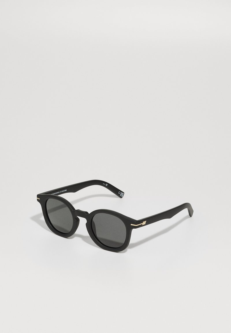 Zwarte zonnebril met een matte afwerking, ronde glazen, dunne zwarte veren en gouden metalen accenten op de scharnieren.