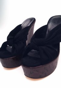 Sandali con tacco neri con un design a nodo sulla parte superiore in tessuto. Base piattaforma in marrone scuro, texturizzata, con una superficie liscia.