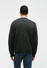 Σκούρο γκρι πλεκτό πουλόβερ με στρογγυλή λαιμόκοψη και ριγωτό τελείωμα, που διαθέτει υφή και μακριά μανίκια. Φοριέται με μπλε τζιν.