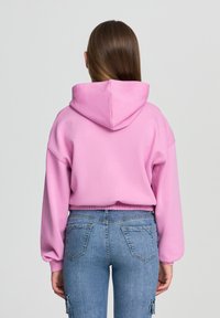 Felpa rosa con una vestibilità morbida e cappuccio, abbinata a jeans blu. Il tessuto sembra morbido con vita e polsini a coste. Nessun motivo visibile.