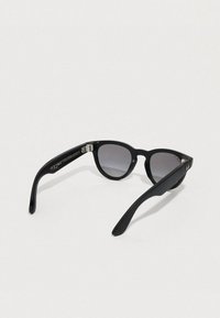 Gafas de sol negras con montura redonda, lentes degradadas y textura mate. Incluye un detalle metálico en la patilla con detalles de la marca.