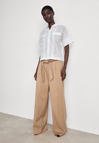 White short-sleeve button-up shirt with lace detailing, paired with beige high-waisted wide-leg trousers featuring a tied waistband.
