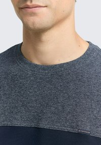 Granatowy sweter z okrągłym dekoltem, z teksturowaną górną częścią, gładką dolną częścią oraz małą metką z logo na dolnym lemie.