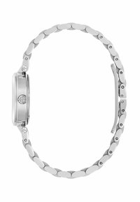 Ceas de mână din metal argintiu, cu brățară din lanț oval și carcasă rotundă, văzut din lateral, evidențiind detalii despre coroana și închizătoare.