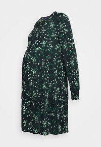 Vestido de maternidad negro con un patrón floral en tonos blancos y verdes, mangas largas, escote redondo y dobladillo en capas.
