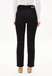 Jean denim noir taille haute, avec deux poches arrière et une étiquette de marque sur la ceinture. Texture lisse, coupe droite.