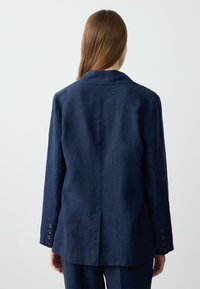 Granatowa lniana marynarka z klasycznym kołnierzem, długimi rękawami, sześcioma guzikami przy mankietach oraz rozcięciem z tyłu dla zwiększenia swobody ruchów.