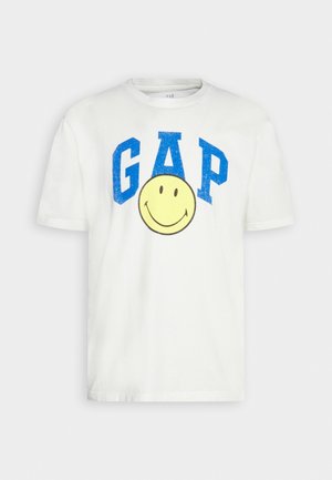 Hvid T-shirt med korte ærmer med blå teksten "GAP" og et gult smiley ansigt centreret under teksten foran.