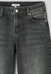 Jean en denim noir avec une taille mi-haute, présentant une fermeture à bouton à l'avant, deux poches latérales et une texture légèrement décolorée.