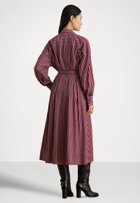 Rød- og hvitstripet kjole med belte i midjen, lange puffede ermer og knappet mansjett, kombinert med knelang svarte støvletter med hæl.