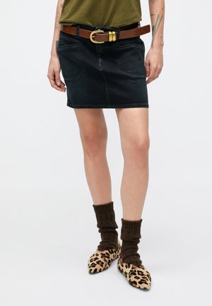 Sort denimnederdel med forlommer, suppleret med et brunt bælte med en guldlås, båret med brune strikkede sokker og leopardmønstrede sko.