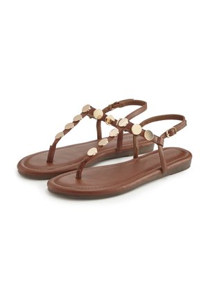 Braune flache Sandalen mit T-Riemen-Design, Knöchelriemchen und goldenen runden Verzierungen an den Riemen.