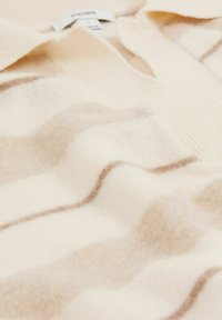 Beige uldblandest trøje med V-hals, blød tekstur og bølgede brune striber over stoffet. Etiketten er synlig ved kraven.