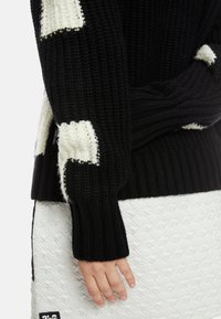 Strickpullover in Schwarz mit weißen Mustern; gerippte Bündchen und Saum, strukturierter Stoff, kombiniert mit einem weißen gemusterten Rock.