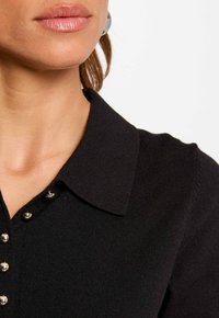 Il maglione con colletto nero presenta un design a maglia testurizzata con bottoni argentati al collo, accentuando un aspetto pulito e rifinito.