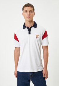 Hvid polo skjorte med marineblå krave, røde og hvide ærmer samt et broderet hundegraphic på brystet. Lavet af bomuld og har et klassisk design.
