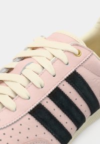 Ροζ δερμάτινο αθλητικό παπούτσι με κρέμ κορδόνια, μαύρες σουέτ ρίγες, διάτρητες λεπτομέρειες και χρυσές μεταλλικές οπές. Επίπεδη λαστιχένια σόλα.