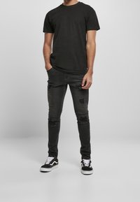 Musta puuvillainen T-paita ja kuluneet mustat farkut, joissa on repaleisia yksityiskohtia. Yhdistetty mustavalkoisiin lenkkareihin, kokonaisuutena rento asu.