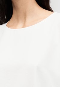 Tissu blanc et lisse avec un col rond qui serre légèrement le cou. La texture semble douce et légère. Aucun motif ni imprimé visible.