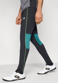 Μαύρο αθλητικό κολάν με τυρκουάζ διακοσμητικές λεπτομέρειες από δίχτυ και λωρίδες πλαϊνές σε νέον πράσινο χρώμα. Το σύνολο συνδυάζεται με λευκά αθλητικά παπούτσια. Ομαλή, εφαρμοστή υφή.