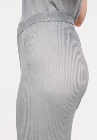 Γκρι ριγωτό φόρεμα κατασκευασμένο από ελαφρύ ύφασμα. Διαθέτει εφαρμοστή σχεδίαση, ζώνη στη μέση και λεία, ελαφρώς διάφανη υφή.