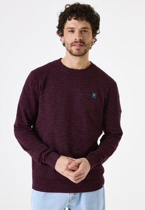 Bordeaux brei sweater met een ronde halslijn, geribde manchetten en zoom. Voorzien van een klein blauw logo-patch op de borst. Klassieke pasvorm.