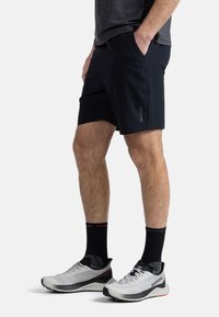 Černé sportovní šortky vyrobené z lehkého materiálu se bočními kapsami, spárované se šedými běžeckými botami s černými akcenty a designem.