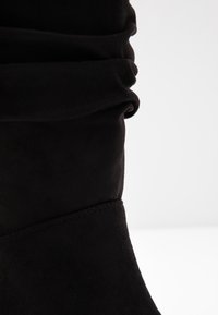 Mustat mokkanahkaiset nilkkurit, joissa on lörpöttävä muotoilu; niissä on sileä pinta ja näkyvät saumat sivuilla.