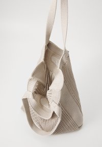 Beige vævet tote taske med mesh-design, struktureret krop og to robuste skulderremme. Har en indvendig lomme til organisering.