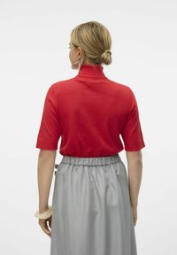 Top rosso a maniche corte con colletto alto, abbinato a una gonna grigia chiara con vita arricciata. Texture liscia con minimi dettagli.