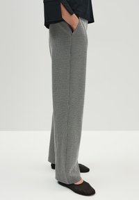 Gray and white patterned wide-leg trousers featuring front pockets and a smooth texture. Worn with black flat shoes, showing a casual style.