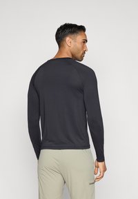 Melnas garajiem piedurknēm sporta krekls ar apaļu kaklu, gluda tekstūra un pieguļošs dizains, attēlots no aizmugures uz vienkārša fona.