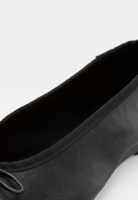 Černá plochá bota vyrobená z hladké kůže s kulatou špičkou, jemným prošíváním a flexibilním elastickým lemem pro pohodlí.