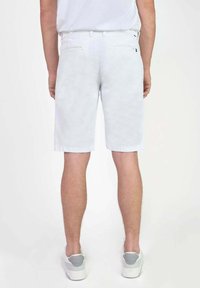 Witte denim shorts met een rechte snit, twee achterzakken en een omgeslagen zoom, gecombineerd met witte sneakers. Gladde textuur, minimale ontwerpdetails.