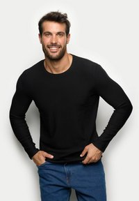 Czarna koszulka z długim rękawem i okrągłym dekoltem, wykonana z gładkiego materiału, w zestawie z niebieskimi dżinsami.